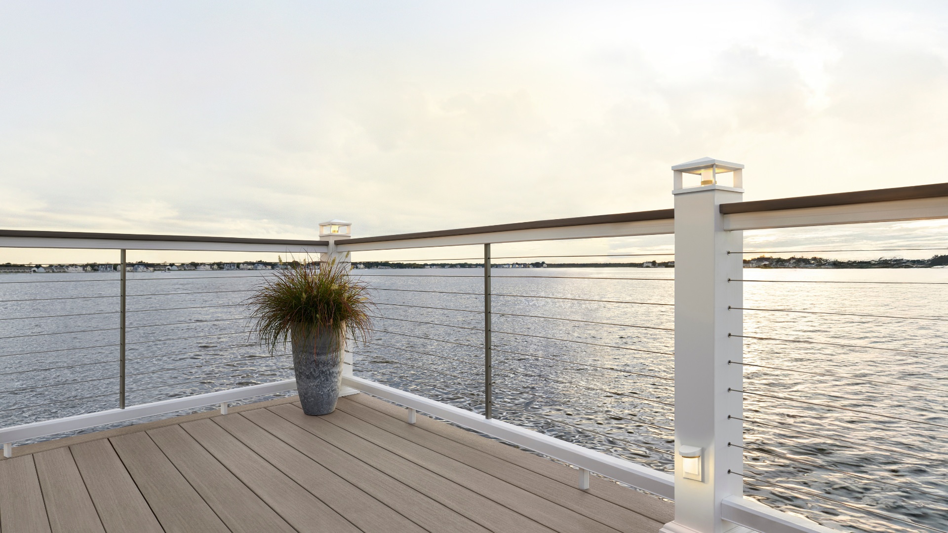 Light color Timbertech deck with cable railing at sunset overlooking a lake. This image is promoting custom deck design by Deck Teck