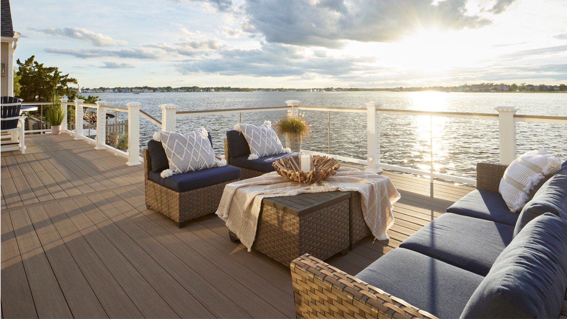 Mahogany color Timbertech deck with modern couches at sunset overlooking a lake. This image is promoting custom deck design by Deck Teck