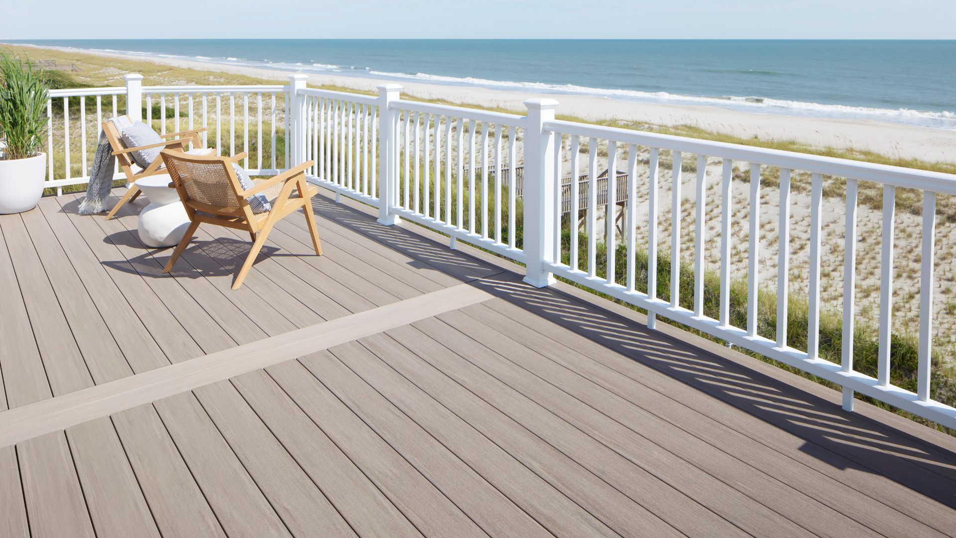 Light tan Timbertech decking with white railing overlooking a sunny beach. This image is promoting custom deck design by Deck Teck