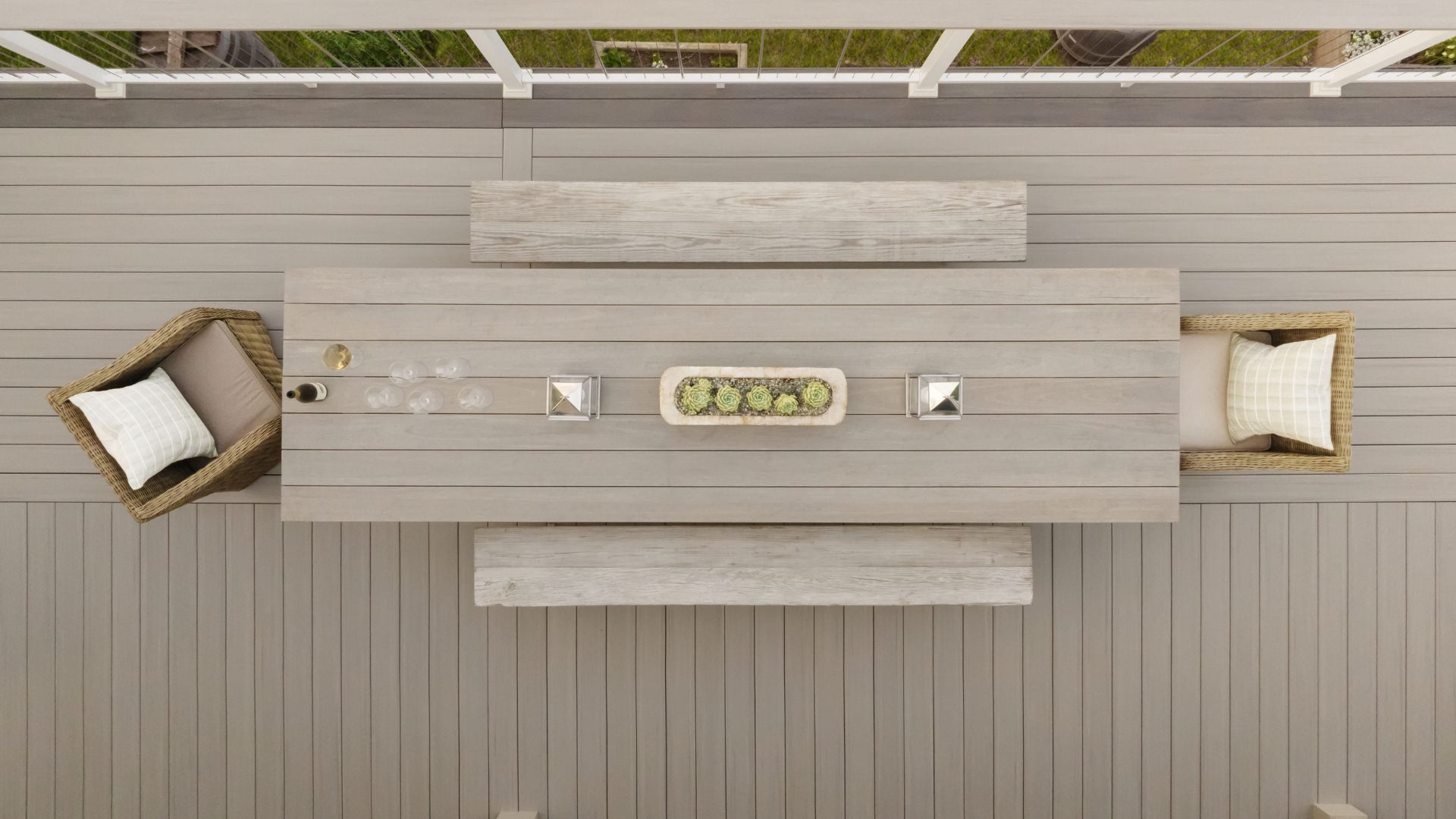 Overhead view of grey Timbertech decking, matching table and bench seating, wicker end chairs with elegant pillows, and vertical cable railing. This image is promoting custom deck design by Deck Teck